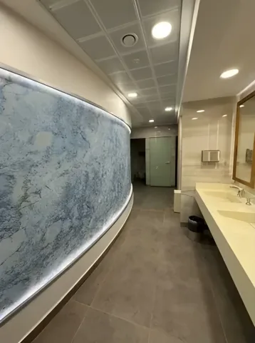 Işıklı kavisli duvar ve lavabo tezgâhı bulunan ıslak hacim