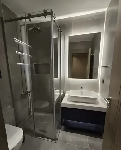 Cam duş kabinli, gri kaplamalı banyo